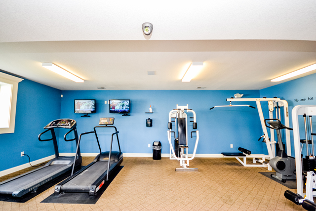 Small fitness room with blue walls, two treadmills, weight machines, and wall-mounted TVs